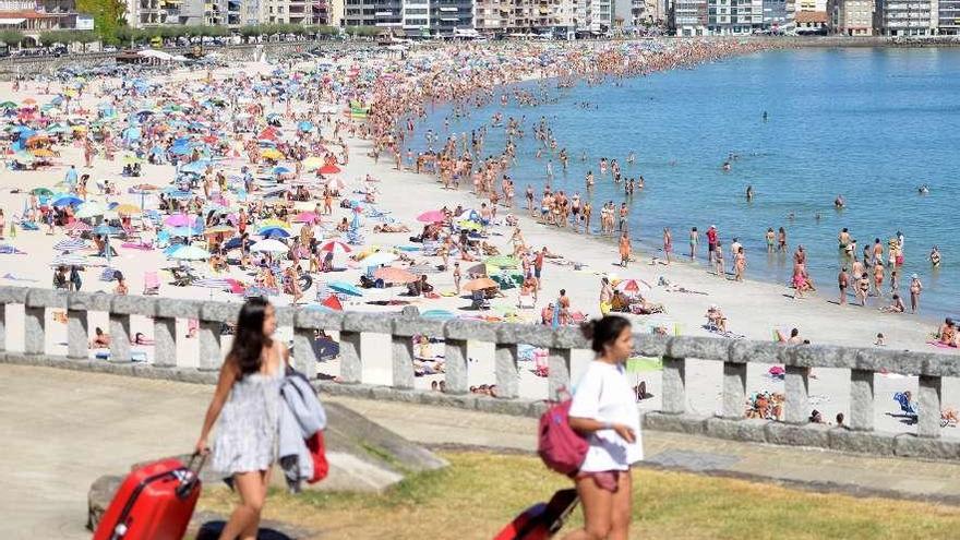 Dos turistas caminan con sus maletas frente a la playa de Silgar.