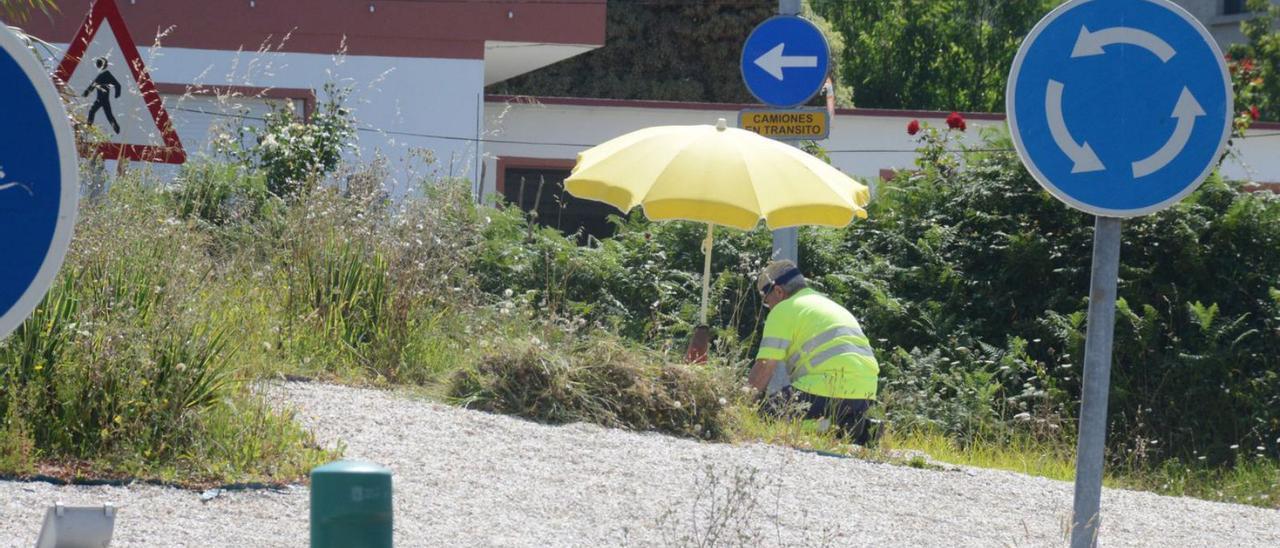 Un operario, trabajando, ayer, en una rotonda de Cangas, en la PO-551, cubierto con una sombrilla.  | // G.N.