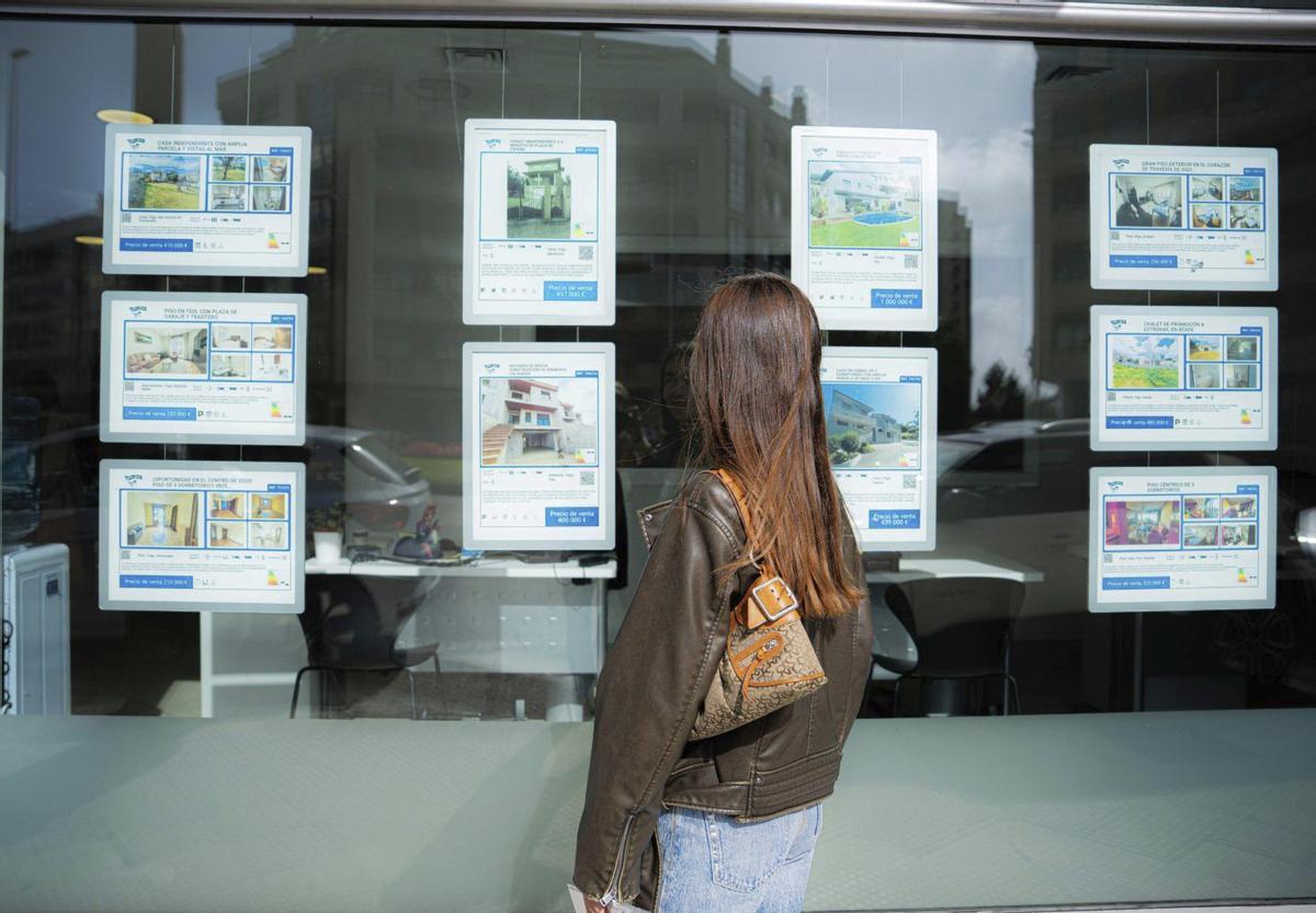 Una joven mira las ofertas de pisos en el escaparate de una inmobiliaria. |  Pedro Mina