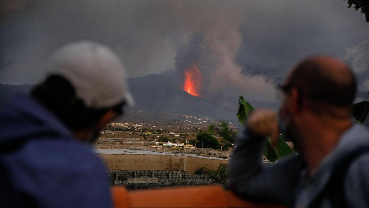 Dos personas observan al volcán de Tajogaite en plena erupción.