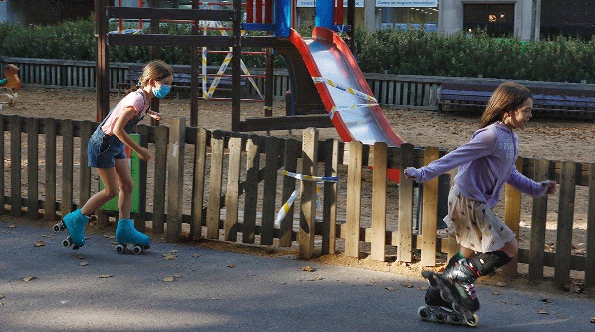 Dos niñas patinan junto a un parque con los columpios precintados, en Barcelona, el 17 de junio.