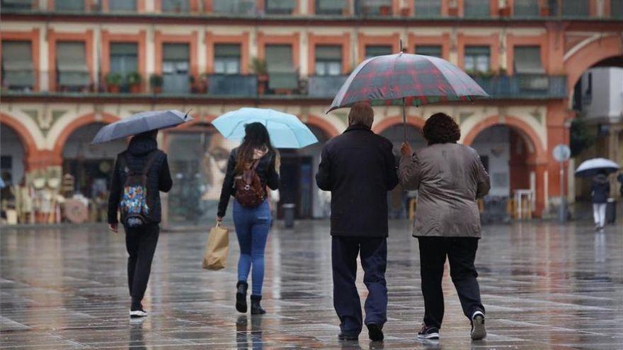 Varias personas se resguardan de la lluvia a su paso por la plaza de la Corredera, en Córdoba capital.