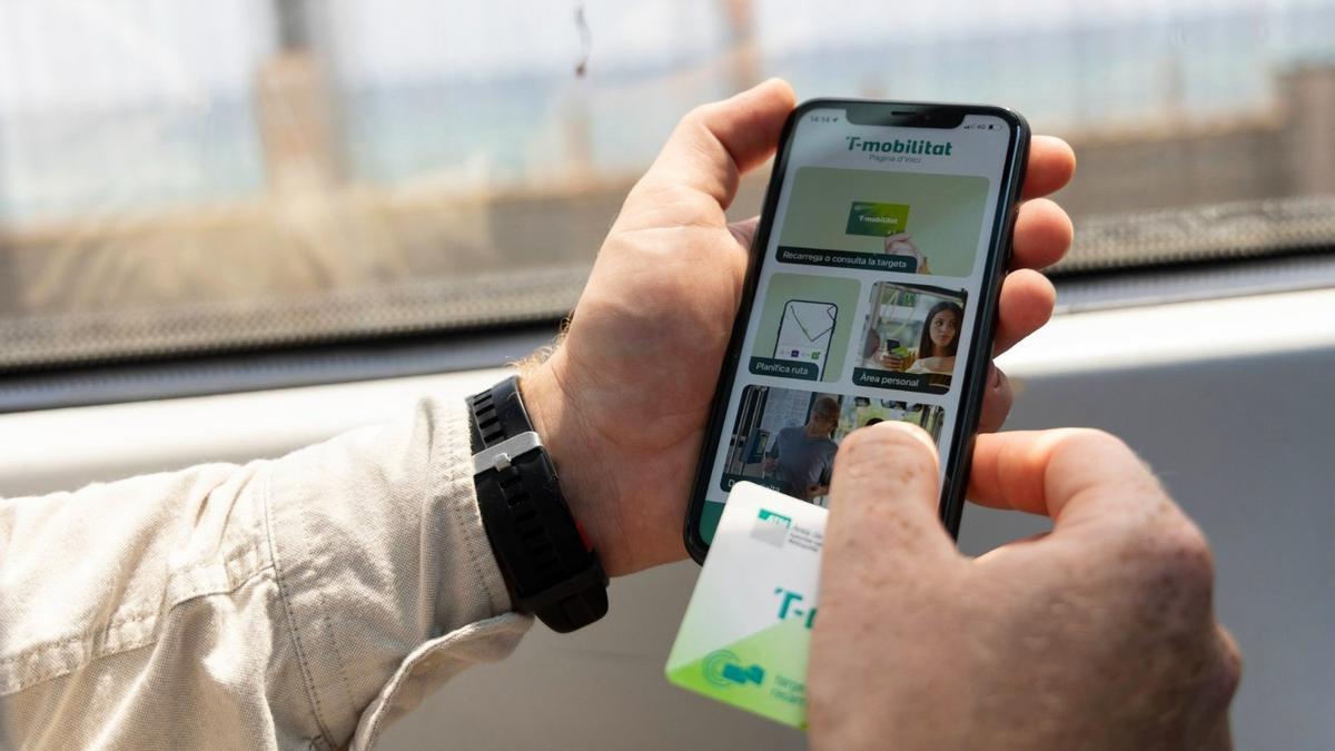 Una persona sostiene una T-Mobilitat de cartón mientras utiliza la 'app' de T-Mobilitat en su teléfono