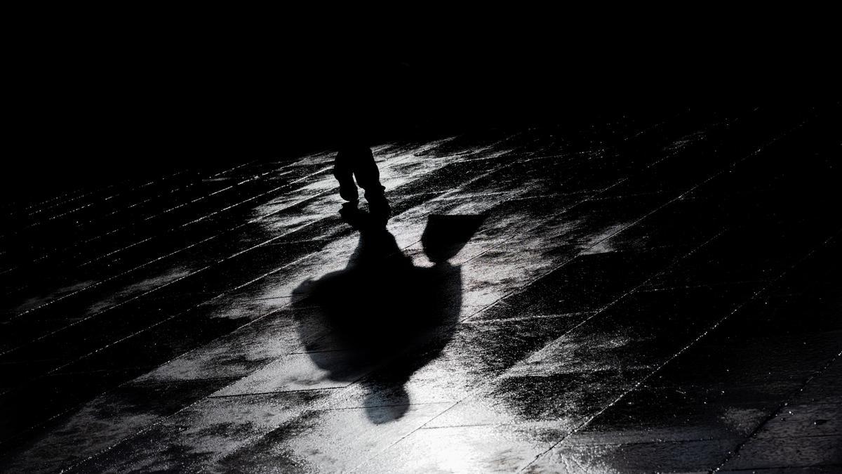 Silhouette im Licht: Der Schatten eines Mannes auf einer Straße nach dem Regen,