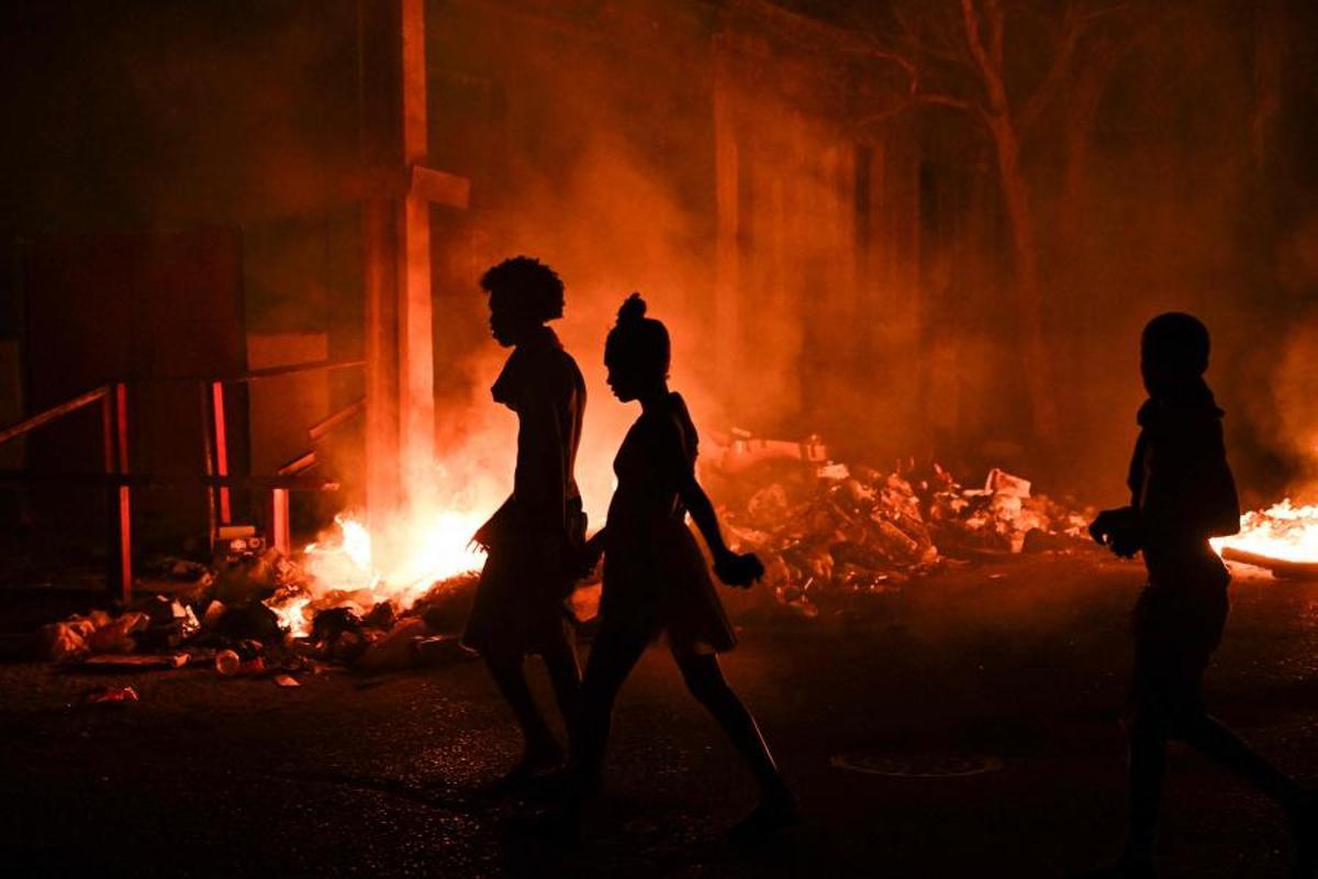 Personas caminan junto a un fuego encendido por manifestantes durante una protesta contra la falta de energía y los apagones en el barrio de Lawton, en La Habana, Cuba, el 14 de mayo de 2026. El gobierno cubano atribuyó a Estados Unidos la situación “particularmente tensa” de su red eléctrica, mientras el este del país sufrió otro corte generalizado ese mismo día. Washington ha ofrecido nuevamente 100 millones de dólares en ayuda, que el gobierno de la isla se muestra “dispuesto” a considerar.