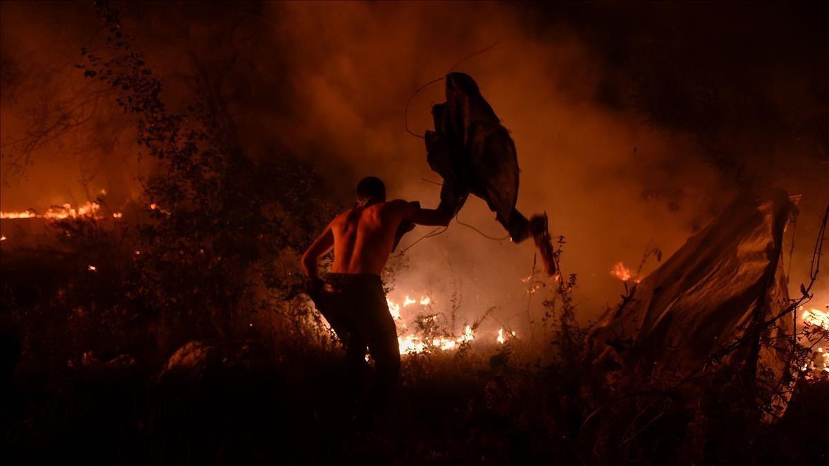 Un joven intenta sofocar el fuego con lo que puede.