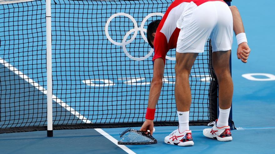 El tenista Novak Djokovic recogiendo una de las raquetas que había tirado al suelo.