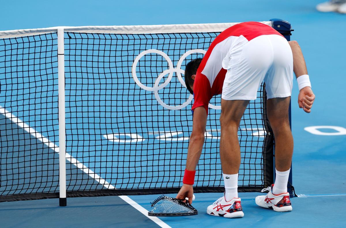 El tenista Novak Djokovic recogiendo una de las raquetas que había tirado al suelo.