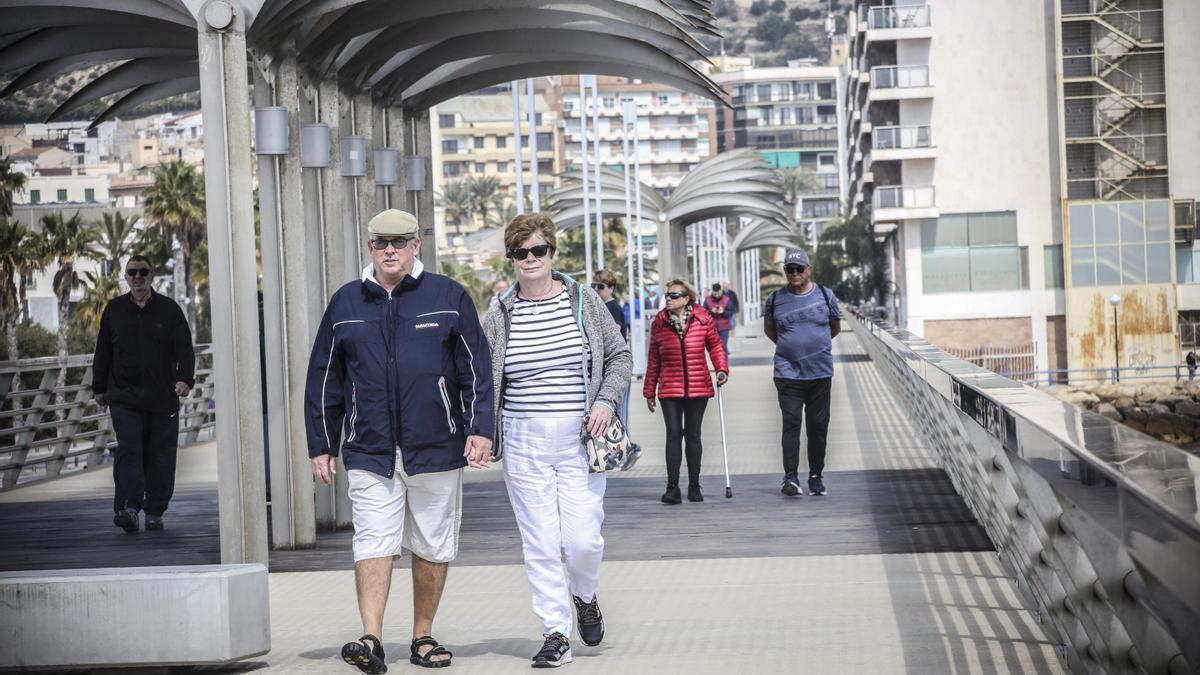 Un pareja de turistas británicos paseando por el paseo volado del puerto de Alicante