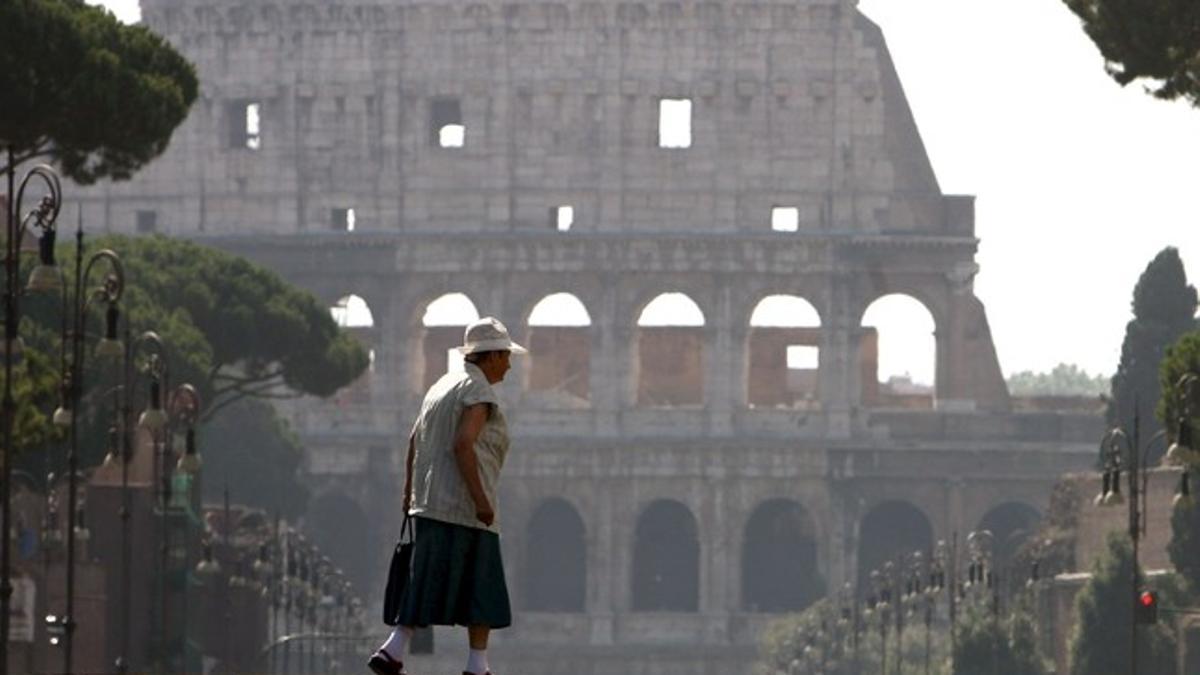 Una mujer pasea por el Foro Imperial ante el Coliseo de Roma.