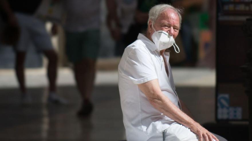 Un hombre descansa en un banco de la malagueña calle Larios con una parte de su mascarilla descolgada.