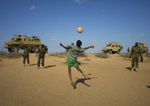 Un niño juega al fútbol con miembros del ejército de Uganda