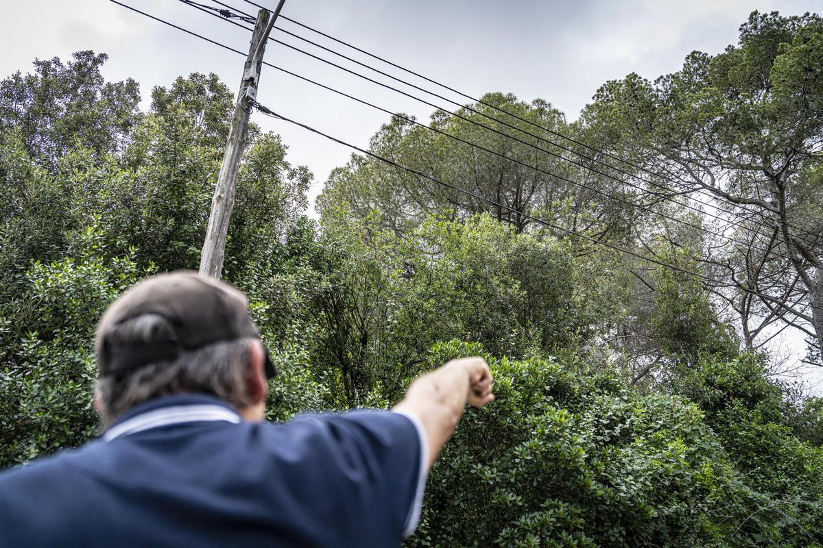 Un vecino de Torre Baró señala los cables de la luz colgados en postes del barrio, en Barcelona.