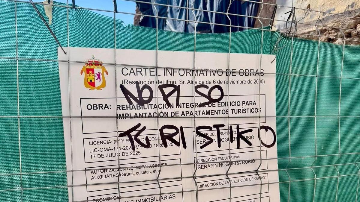 El cartel de la obra de la calle Caleros, cubierto por una pintada contra la promoción turística.