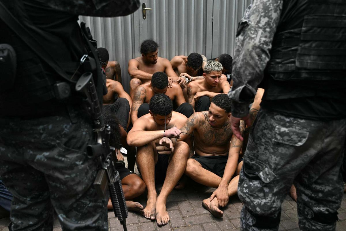 TOPSHOT - Police officers guard alleged criminals arrested during the Operacao Contencao (Operation Containment) at the Vila Cruzeiro favela, in the Penha complex, in Rio de Janeiro, Brazil, on October 28, 2025. At least 2,500 security forces agents took part in an operation to arrest drug traffickers from the Comando Vermelho (CV), which resulted in 64 people dead, authorities reported. (Photo by Mauro PIMENTEL / AFP)