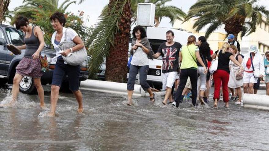 Los turistas cruzan, hasta con los zapatos en la mano, por el riachuelo que se formó en Maspalomas ayer. | sergio pérez