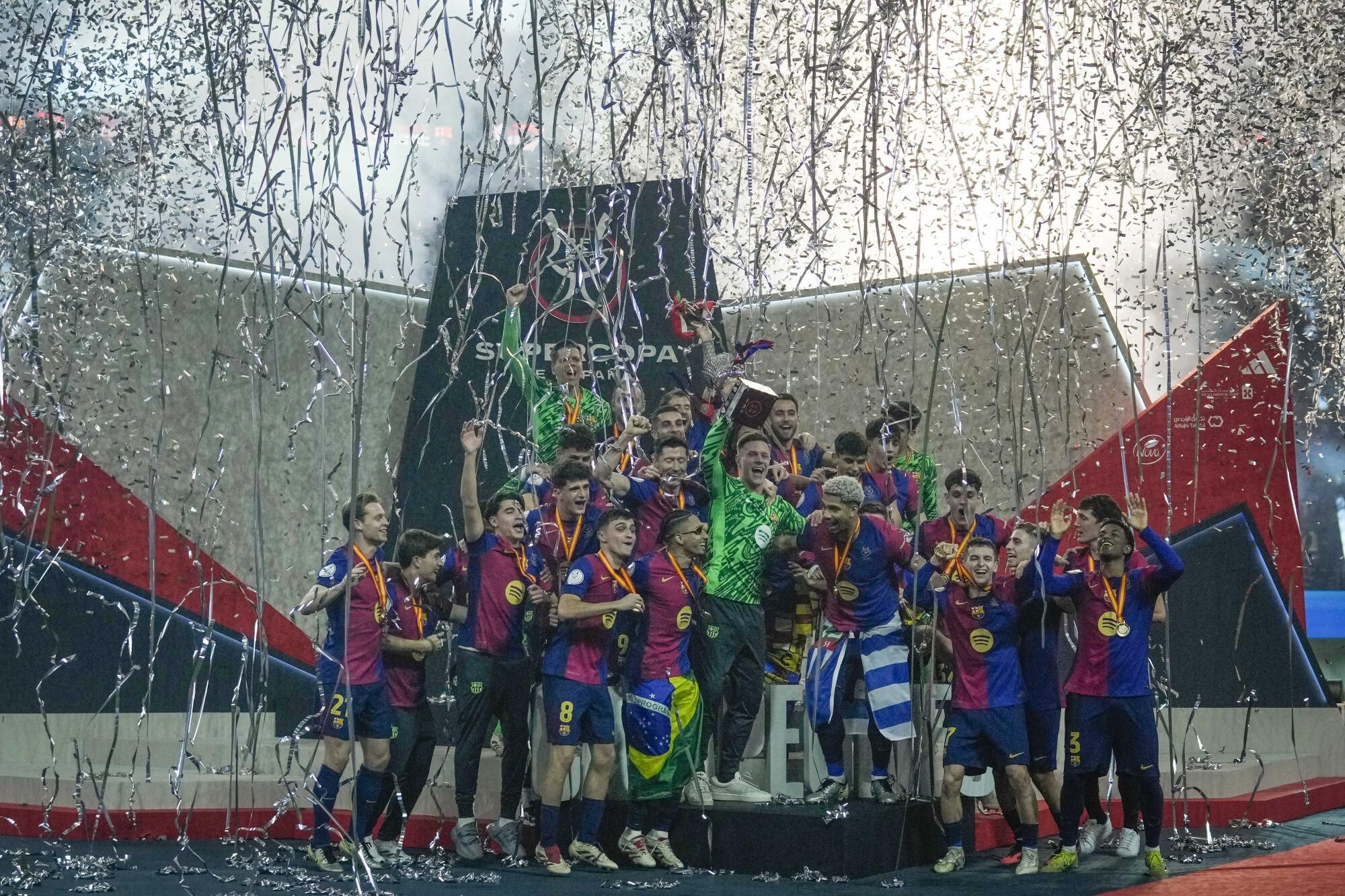 Barcelona players celebrate with their team's trophy of the Spanish Super Cup after the final soccer match between Real Madrid and Barcelona at King Abdullah Stadium in Jeddah, Saudi Arabia, Monday, Jan. 13, 2025. (AP Photo/Altaf Qadri). EDITORIAL USE ONLY/ONLY ITALY AND SPAIN