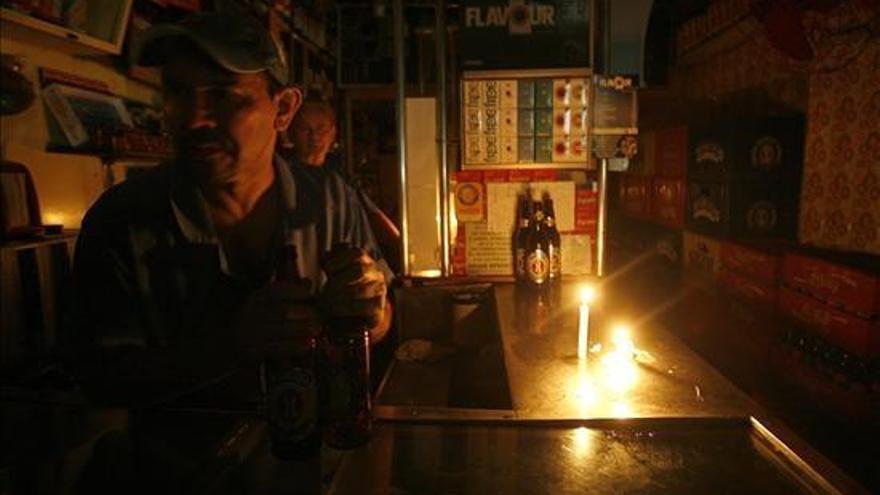 Un señor atiende su bar a la luz de una vela.