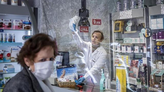Una farmacéutica limpia la mampara de plástico de su comercio
