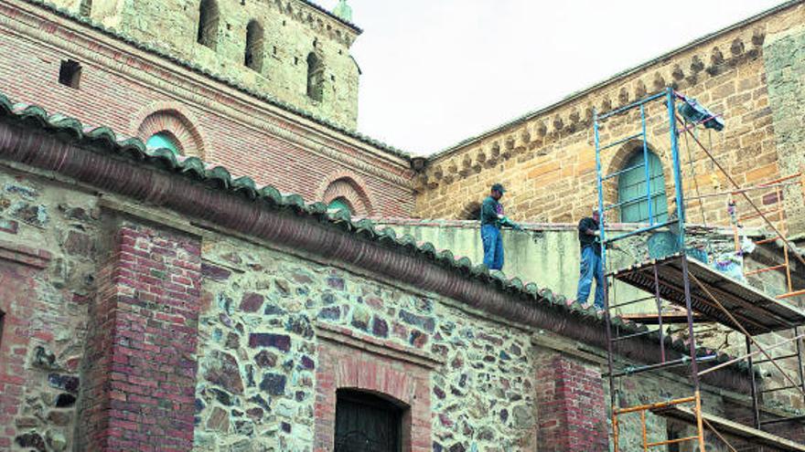 Dos trabajadores retiran el enfoscado de una de las paredes de la iglesia de Santa María del Azogue.