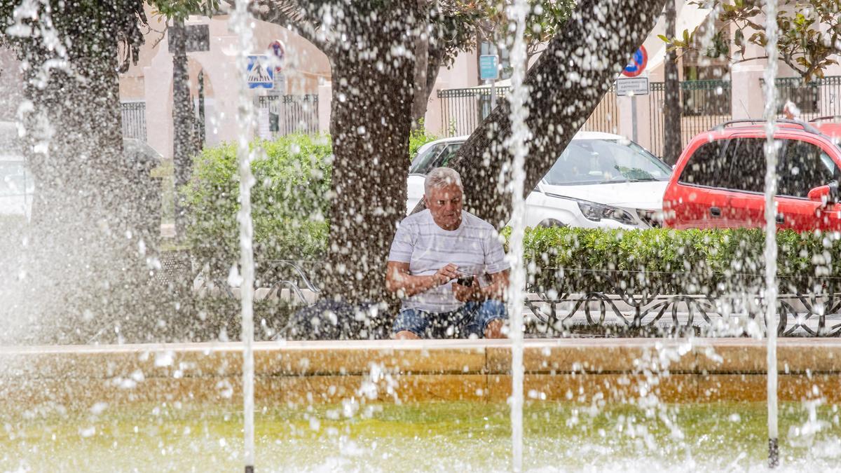 Un hombre consulta el móvil protegiendose del calor junto a una fuente de Orihuela, una de las sartenes de la provincia