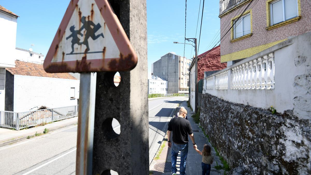 Un hombre camina con una niña por el lugar donde se produjo el siniestro, ante una oxidada señal de zona escolar