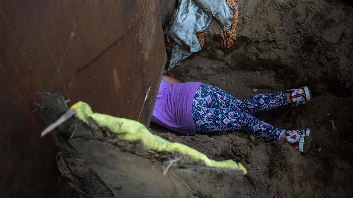 Andrea Nicolle, migrante hondureña,  intenta pasar a EEUU cavando un agujero bajo la valla metálica.