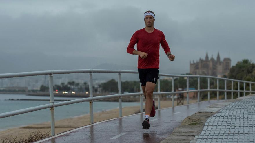 Un hombre corre bajo la lluvia por el paseo de la Playa de Can Pere Antoni.