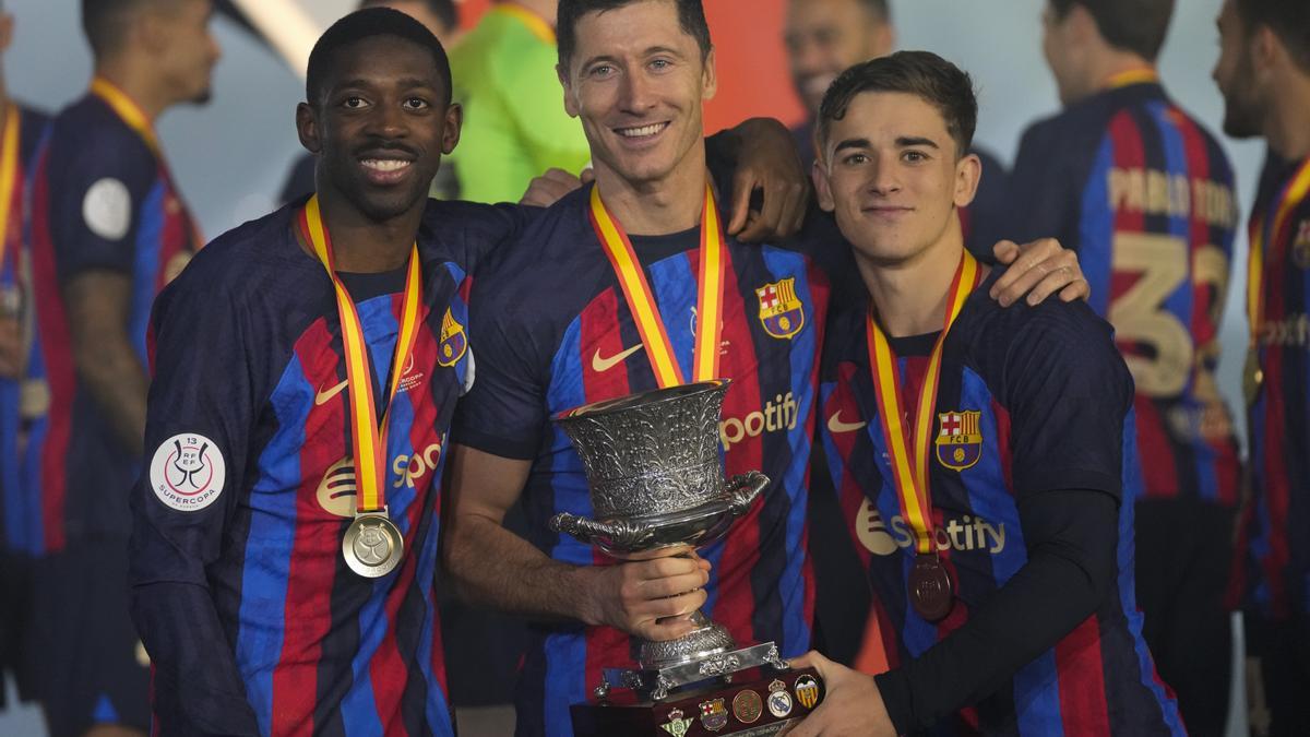 Robert Lewandowski (M) und seine Mitspieler des FC Barcelona freuen sich über einen Pokal nach dem Sieg im Finale des spanischen Superpokals.
