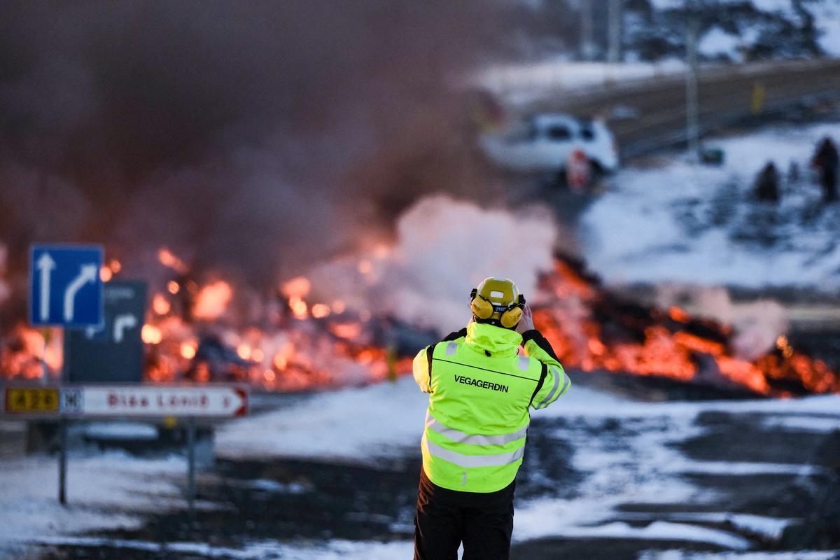 El personal de una agencia de carreteras toma una fotografía mientras se ve lava fundida desbordando la carretera que conduce al famoso destino turístico Laguna Azul cerca de Grindavik, en el oeste de Islandia, el 8 de febrero de 2023.