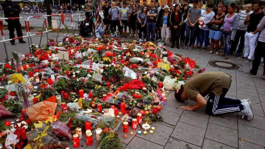 Un hombre reza ante flores y velas depositadas delante del centro comercial Olympia. // Reuters