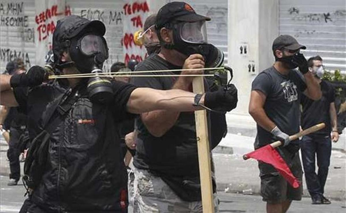Un manifestant apunta amb el seu tirador a un policia antiavalots durant els enfrontaments davant del Parlament grec.