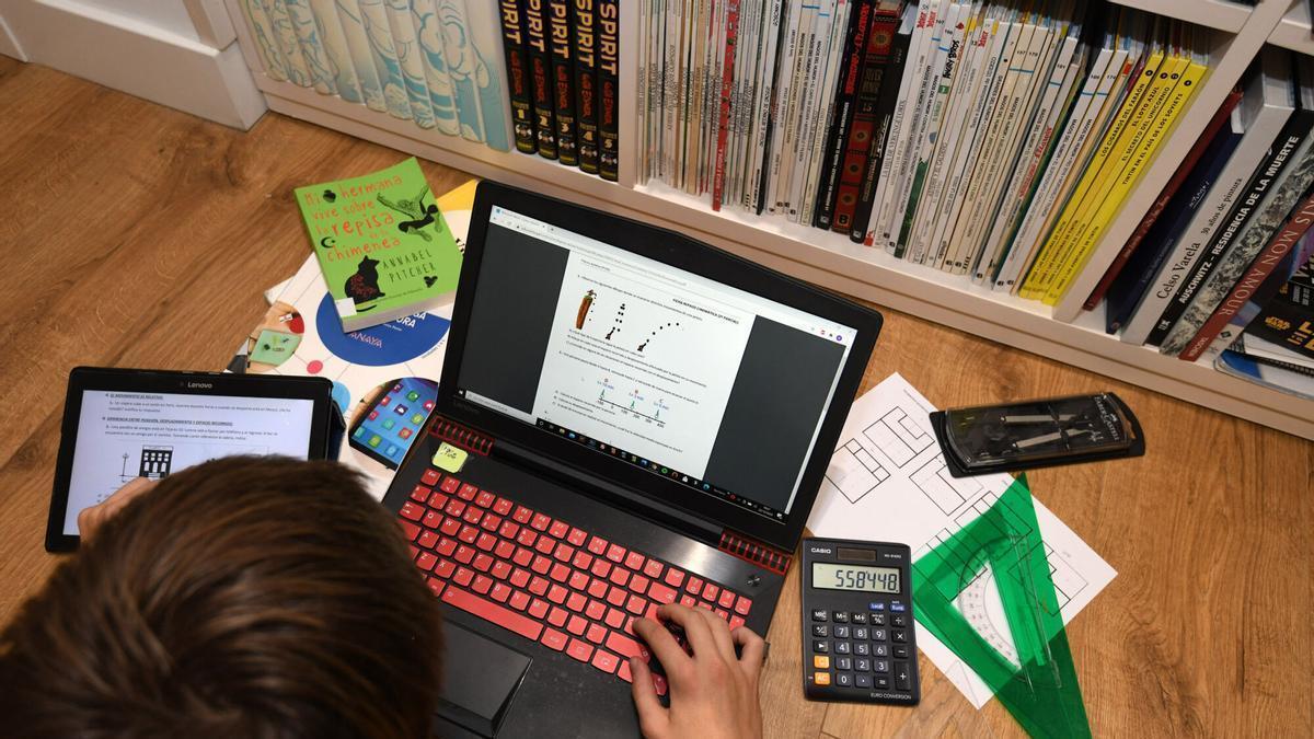 Un joven en edad escolar estudia en su casa con ordenador y tablet.