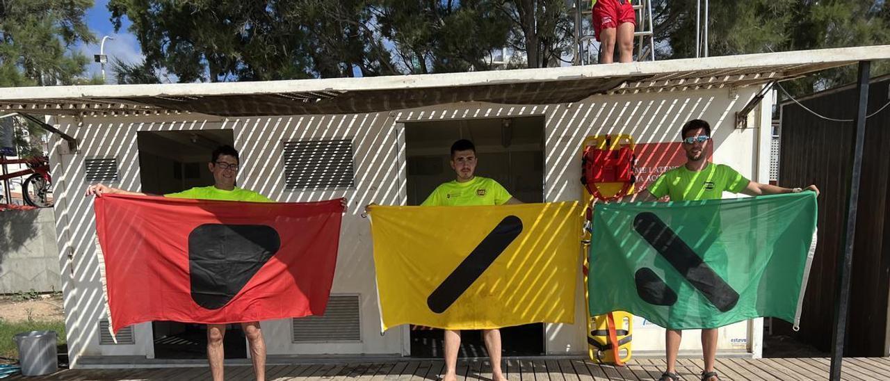 Tres socorristas de Vinaròs sostienen las banderas que permiten a las personas daltónicas conocer el estado del mar.