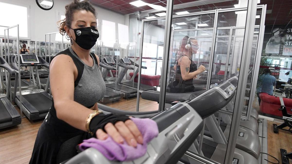 Usuaria de un gimnasio protegida con mascarilla desinfecta una cinta de correr, 19 octubre 2020