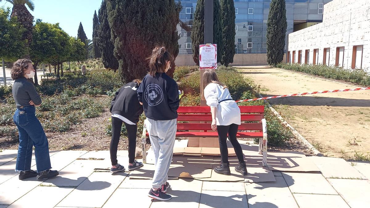 Varias alumnas pintan el banco rojo frente a la Facultad de Comunicación de la UMU.