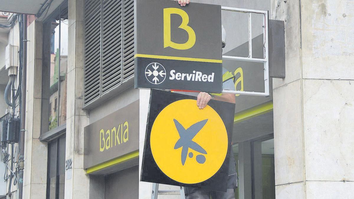 Un operari retira un logotip de Bankia per posar-hi un de CaixaBank en una foto d’arxiu. | ACN