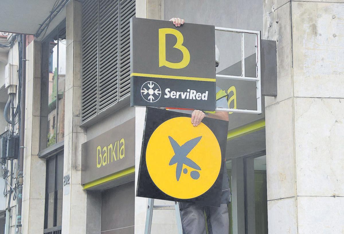 Un operari retira un logotip de Bankia per posar-hi un de CaixaBank en una foto d’arxiu. | ACN