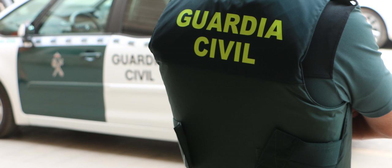 Archivo - Un agente de la Guardia Civil, de espaldas, junto a un vehículo oficial.