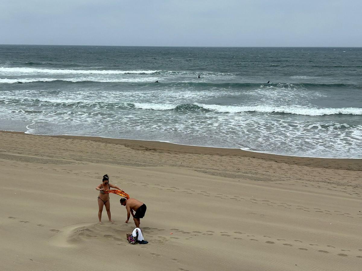 Usuarios finalizando su jornada en la playa de Salinas con surfistas al fondo.