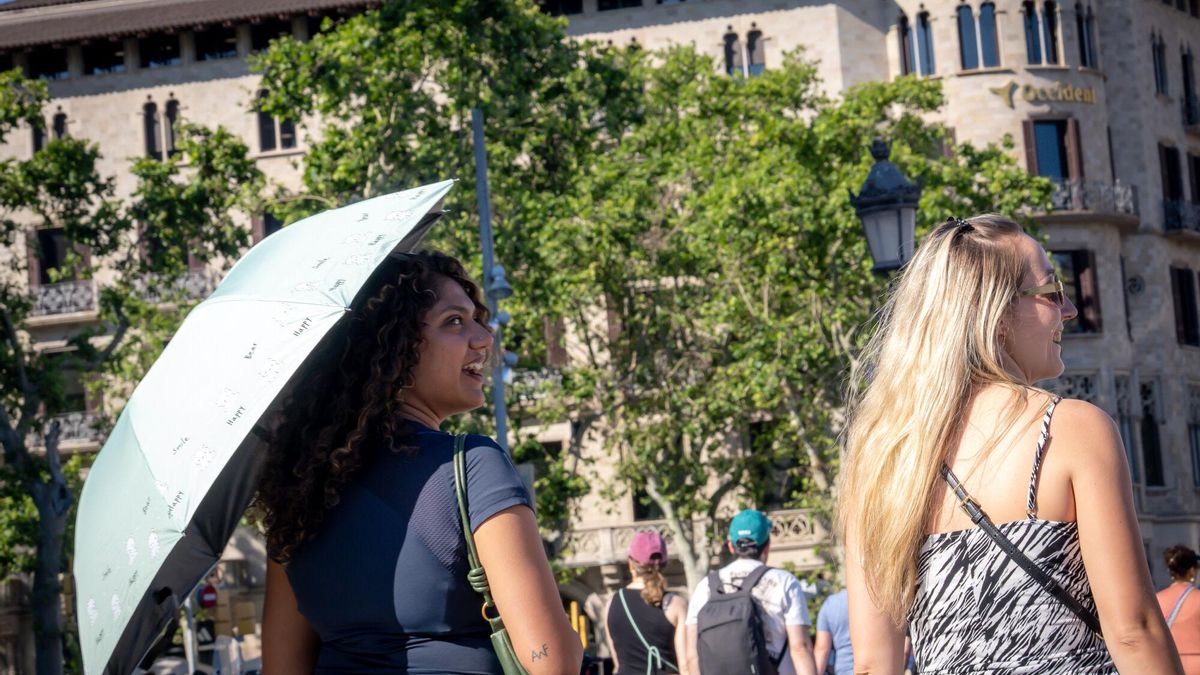 Una mujer se refugia del sol bajo un paraguas durante una jornada de calor en Barcelona.
