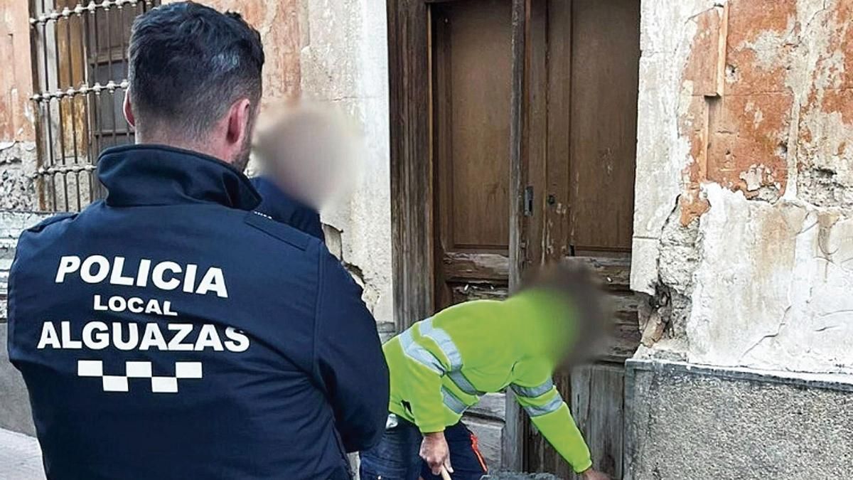 Un agente de la Policía Local de Alguazas mira  cómo un obrero tapia una casa okupada.