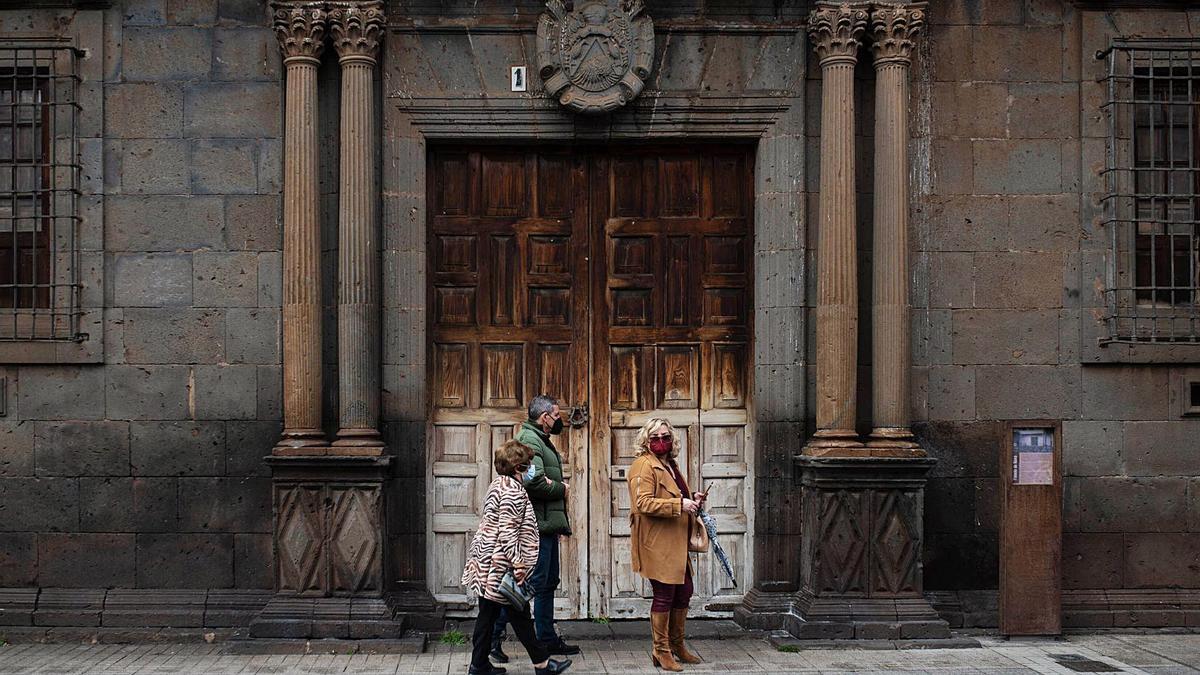 Tres personas pasan frente a la entrada principal del Obispado de La Laguna, en pleno casco histórico.
