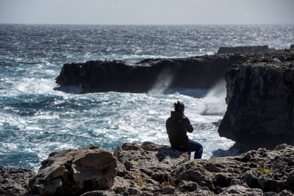 Imagen de archivo de un joven observa romper las olas sobre las rocas.