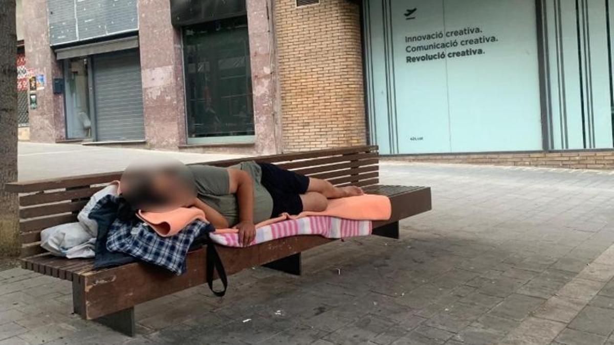 Una persona dorm al passeig de la República de Manresa sobre un banc de fusta