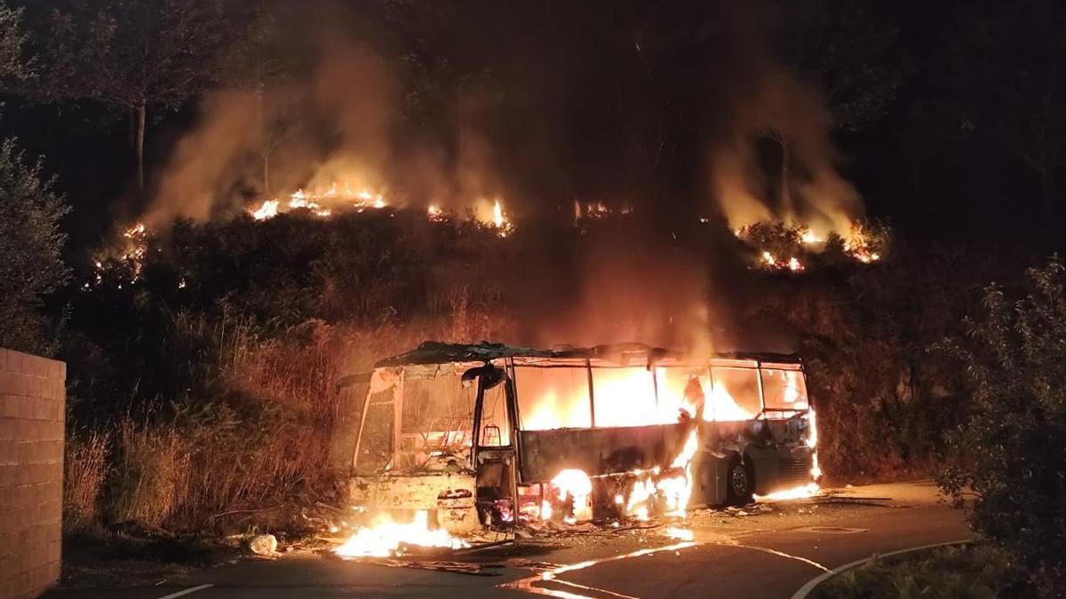 El autobús ardiendo en la parroquia de Verducido, cuyo fuego afectó a zona boscosa.