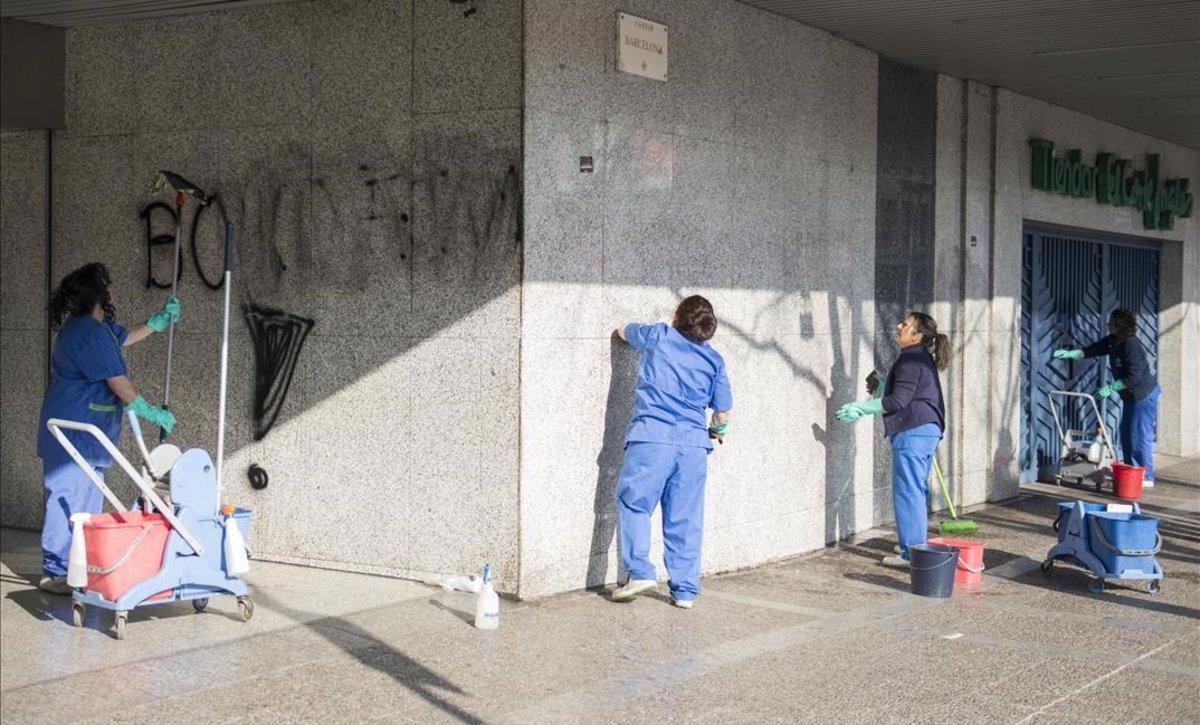 Trabajadores de Hipercor en Girona limpian pintadas realizadas por manifestantes durante la jornada de huelga.
