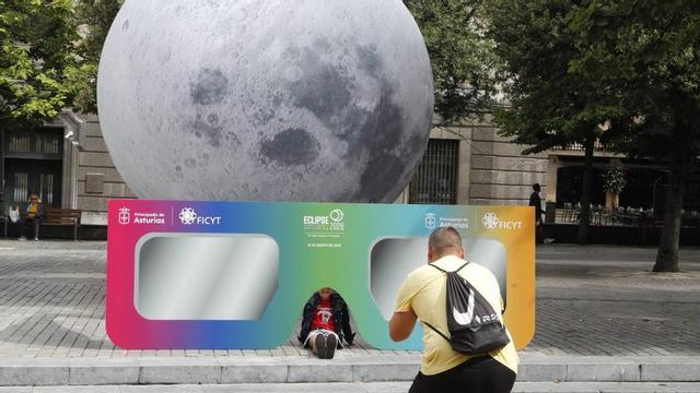 Un hombre fotografía a un niño, en Oviedo, bajo las gafas gigantes para ver el eclipse diseñadas por el Principado con motivo de la campaña de divulgación del fenómeno. | FERNANDO RODRÍGUEZ