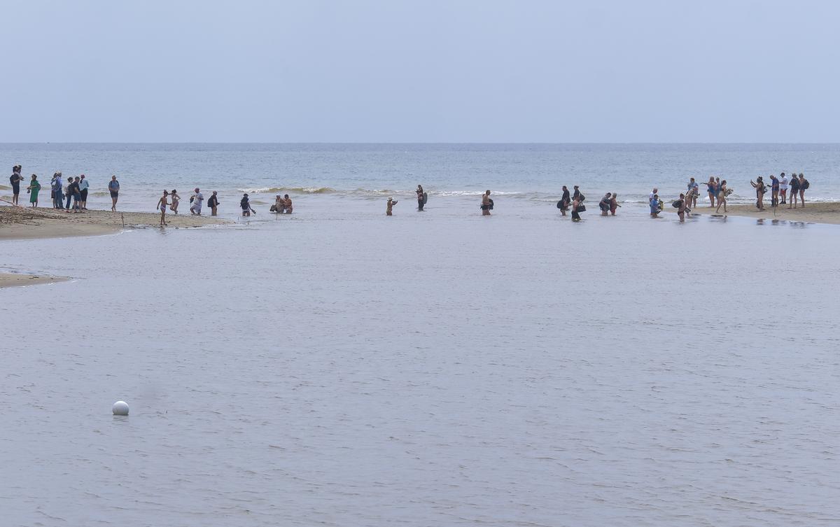 Turistas cruzando el cauce de la salida del agua al mar de la Charca de Maspalomas.