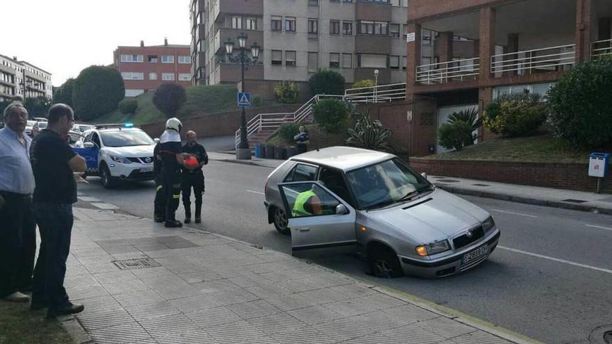 El coche atrapado ayer en el socavón, con los bomberos preparándose para actuar.